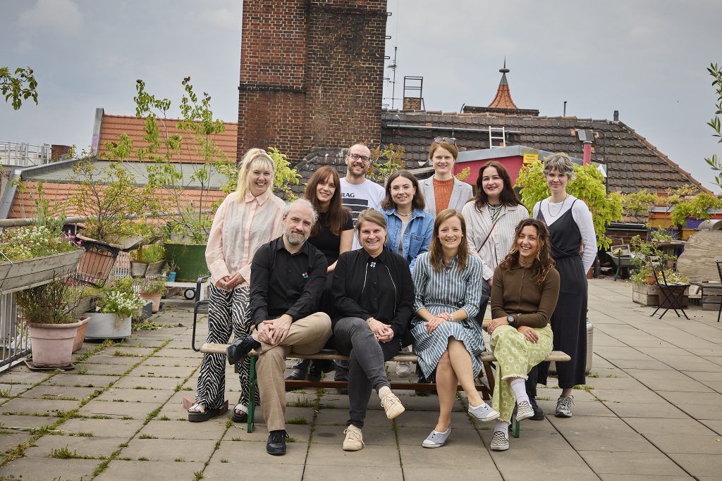 Teamfoto von toneshift. Auf dem Bild sind 11 Personen aus den verschiedenen Organisationen zu sehen, die lachend in die Kamera schauen. Das Foto wurde auf einer Dachterrasse aufgenommen.